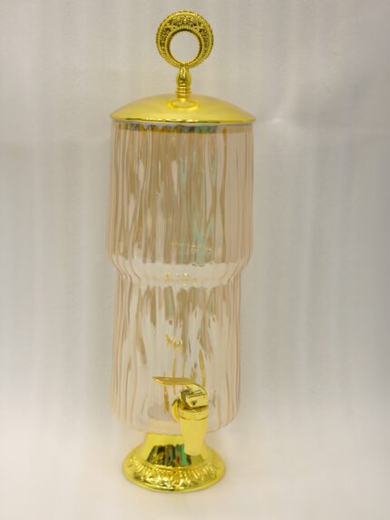 3.5L ribbed pink glass beverage dispenser with ornate gold base, spout, and top handle standing on a kitchen marble countertop
