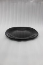 Glossy black 38-piece ceramic dinner set arranged on a rustic wooden dining table near a bright window.