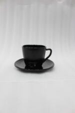 Glossy black 38-piece ceramic dinner set arranged on a rustic wooden dining table near a bright window.