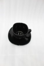 Glossy black 38-piece ceramic dinner set arranged on a rustic wooden dining table near a bright window.