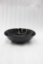 Glossy black 38-piece ceramic dinner set arranged on a rustic wooden dining table near a bright window.