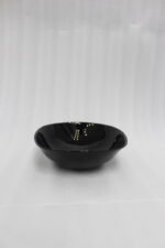 Glossy black 38-piece ceramic dinner set arranged on a rustic wooden dining table near a bright window.