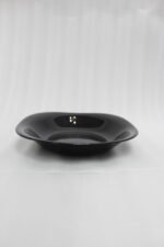 Glossy black 38-piece ceramic dinner set arranged on a rustic wooden dining table near a bright window.