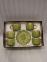 A boxed 6-person green ceramic cup and saucer set featuring textured patterns and gold handles and rims, displayed on a kitchen counter.
