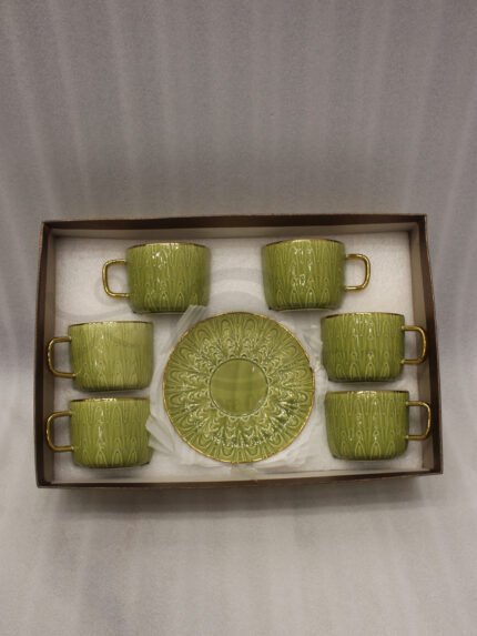 A boxed 6-person green ceramic cup and saucer set featuring textured patterns and gold handles and rims, displayed on a kitchen counter.