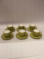 A boxed 6-person green ceramic cup and saucer set featuring textured patterns and gold handles and rims, displayed on a kitchen counter.