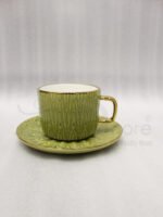 A boxed 6-person green ceramic cup and saucer set featuring textured patterns and gold handles and rims, displayed on a kitchen counter.