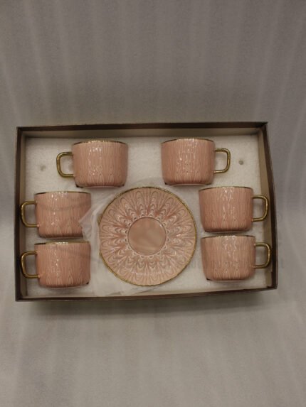 Pink ceramic cup and saucer 6-person set with gold trim inside a gift box on a kitchen counter.