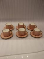 Pink ceramic cup and saucer 6-person set with gold trim inside a gift box on a kitchen counter.