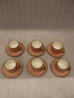 Pink ceramic cup and saucer 6-person set with gold trim inside a gift box on a kitchen counter.