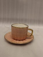Pink ceramic cup and saucer 6-person set with gold trim inside a gift box on a kitchen counter.