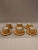 Elegant 6-person beige ceramic tea cup and saucer set with gold handles arranged inside a presentation gift box on a kitchen counter.