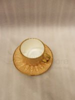 Elegant 6-person beige ceramic tea cup and saucer set with gold handles arranged inside a presentation gift box on a kitchen counter.