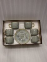 A luxury 6-person sage green ceramic cup and saucer set with gold trim, neatly packed in a gift box on a kitchen counter.
