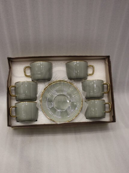 A luxury 6-person sage green ceramic cup and saucer set with gold trim, neatly packed in a gift box on a kitchen counter.