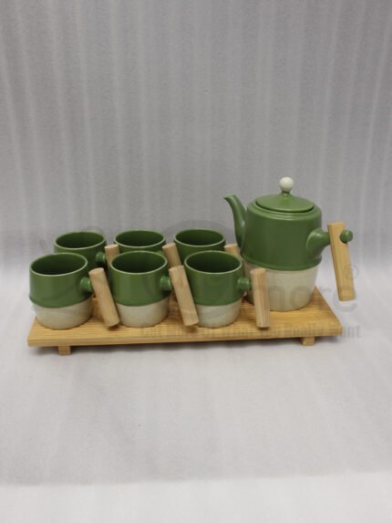 A modern green and cream ceramic tea set for 6 persons featuring wooden handles and a wooden tray on a kitchen counter.