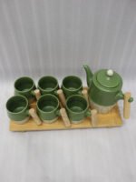 A modern green and cream ceramic tea set for 6 persons featuring wooden handles and a wooden tray on a kitchen counter.
