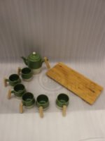 A modern green and cream ceramic tea set for 6 persons featuring wooden handles and a wooden tray on a kitchen counter.