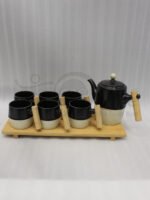 "A modern 6-person ceramic tea set displayed on a kitchen counter, including a teapot, six cups, and a bamboo serving tray, all featuring matte black and speckled finishes with wooden handles."