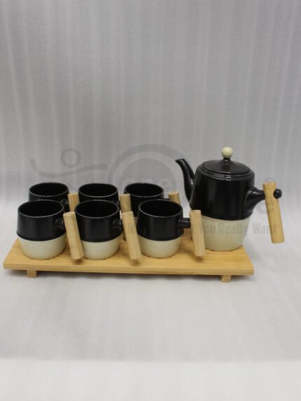 "A modern 6-person ceramic tea set displayed on a kitchen counter, including a teapot, six cups, and a bamboo serving tray, all featuring matte black and speckled finishes with wooden handles."
