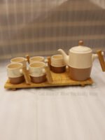 A complete modern tea set for 6 persons, featuring cream and mocha two-tone ceramic teapot and six matching mugs with bamboo handles, neatly organized on two bamboo serving trays on a kitchen counter.