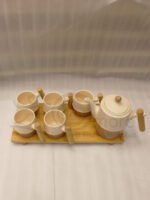 A complete modern tea set for 6 persons, featuring cream and mocha two-tone ceramic teapot and six matching mugs with bamboo handles, neatly organized on two bamboo serving trays on a kitchen counter.