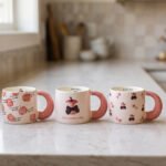 Cream ceramic coffee mug featuring a Snow White apple with a black bow, "Be a princess today" text, and a thick pink rounded handle sitting on a marble kitchen counter.
