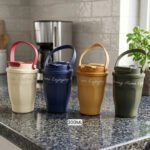Four 300ml portable travel coffee mugs in cream, navy blue, mustard yellow, and olive green with top carrying handles placed on a kitchen countertop.