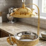 Luxury gold buffet chafing dish with overhead hanging dome lid, stainless steel food pan, and attached serving tongs.