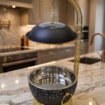 One More luxury matte black and gold hanging lid buffet chafing dish with stainless steel pan on a marble kitchen counter.