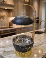 One More luxury matte black and gold hanging lid buffet chafing dish with stainless steel pan on a marble kitchen counter.