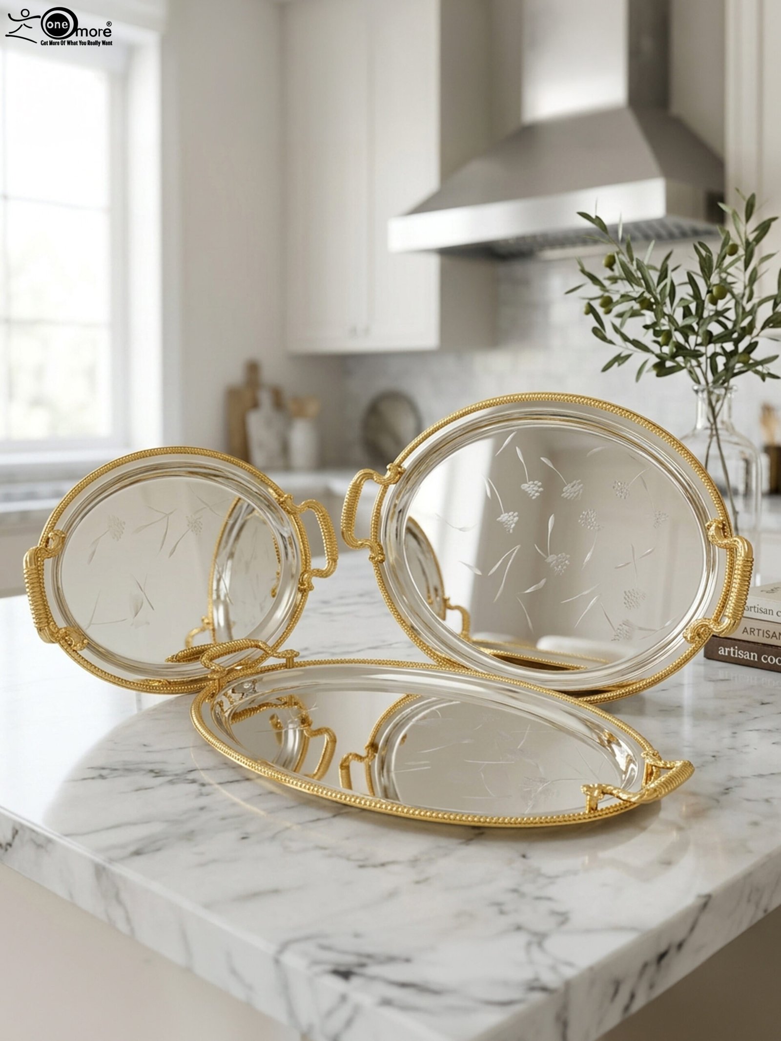 1 Set of three silver mirrored oval serving trays with floral etchings and textured gold handles on a marble countertop.
