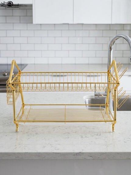 2 tier luxury gold metal dish drying rack with utensil basket, glass holder hooks, and clear drip tray on a kitchen countertop next to a faucet.
