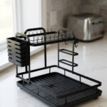 Modern 2-tier black metal dish drying rack with side utensil caddy and bottom drain tray on a kitchen countertop.