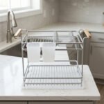 Two-tier silver dish drying rack with wooden side handles, hanging utensil holders, and a plastic drip tray on a kitchen countertop.