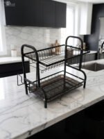 2-tier black metal dish drying rack with utensil holder and drip tray on a marble kitchen countertop