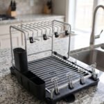 Modern 2-tier stainless steel dish drying rack with integrated knife block, utensil caddy, cup holders, and drainage tray on a granite countertop next to the sink.