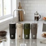 Four 350ml insulated travel coffee mugs in black, beige, olive green, and grey on a kitchen countertop next to coffee beans.