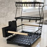 3-tier black wire dish drying rack on a marble countertop with wooden handles, attached utensil holder, and removable drip tray