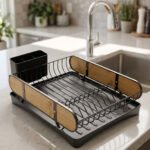 Matte black metal dish drying rack with natural wooden side accents, a black cutlery holder, and a removable drip tray sitting next to a kitchen sink.