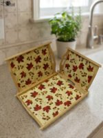 Set of three rectangular wooden serving trays featuring a red maple leaf and berry print displayed on a light kitchen countertop.