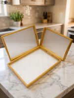 Set of three natural wood nesting serving trays with cutout handles and smooth white inner bases displayed on a kitchen marble countertop.