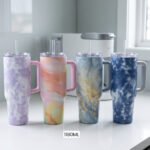 Four 1180ml insulated stainless steel travel tumblers with handles and straws in lavender, peach, blue-gold, and navy marble patterns on a kitchen counter.