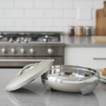 Cream and stainless steel insulated thermal hotpot casserole dish with lid resting on a granite kitchen countertop.
