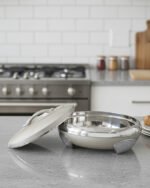 Cream and stainless steel insulated thermal hotpot casserole dish with lid resting on a granite kitchen countertop.