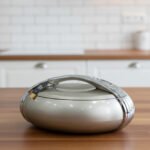 Modern grey insulated hotpot casserole with polished chrome handle on a wooden kitchen countertop