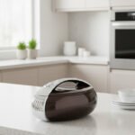 Glossy brown oval insulated hotpot casserole with chrome handle on a modern kitchen countertop.