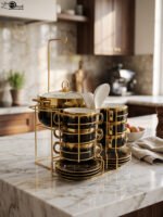 Luxury black and gold ceramic soup set with double-handled cups, covered soup tureen, white spoons, and gold metal display rack on a marble kitchen counter.