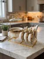 Luxury gradient brown ceramic soup tureen pot with glass lid, gold warmer stand, hanging double-handled soup bowls, saucers, and white spoons set on a wooden dining table.