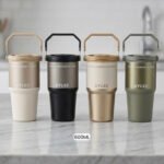 Four UYLEE 600ml stainless steel insulated travel tumblers with folding handles shown in beige, matte black, champagne gold, and olive green on a marble countertop.